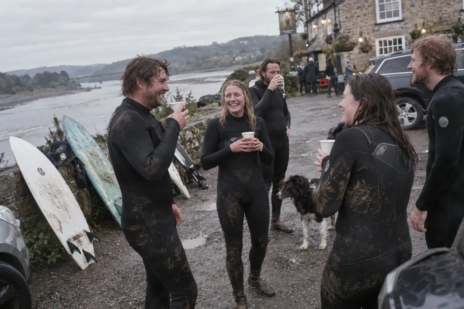 Surfers in wetsuits drink tea next to a pub after surfing the bore