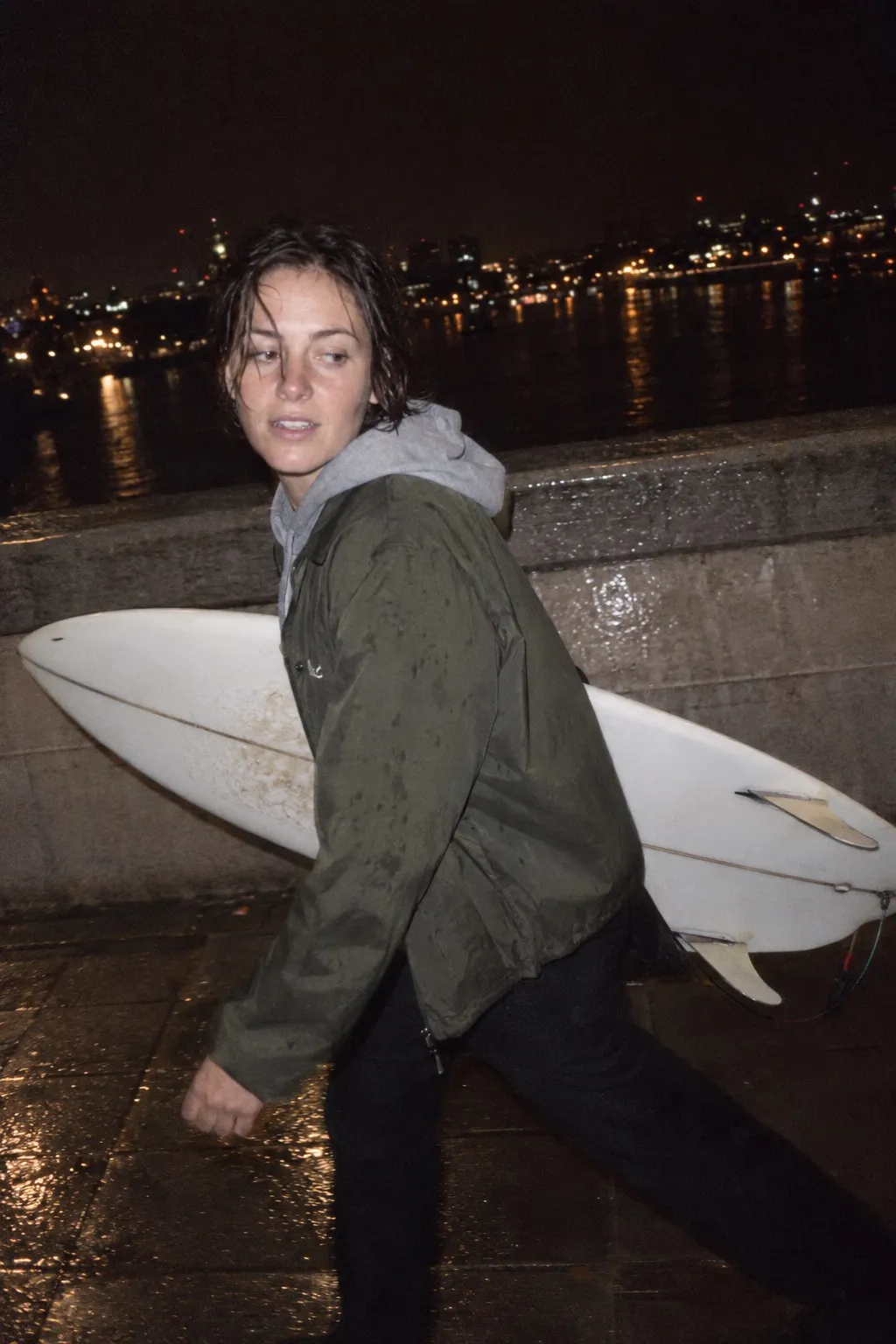 A woman carries a surfboard across Waterloo Bridge at night