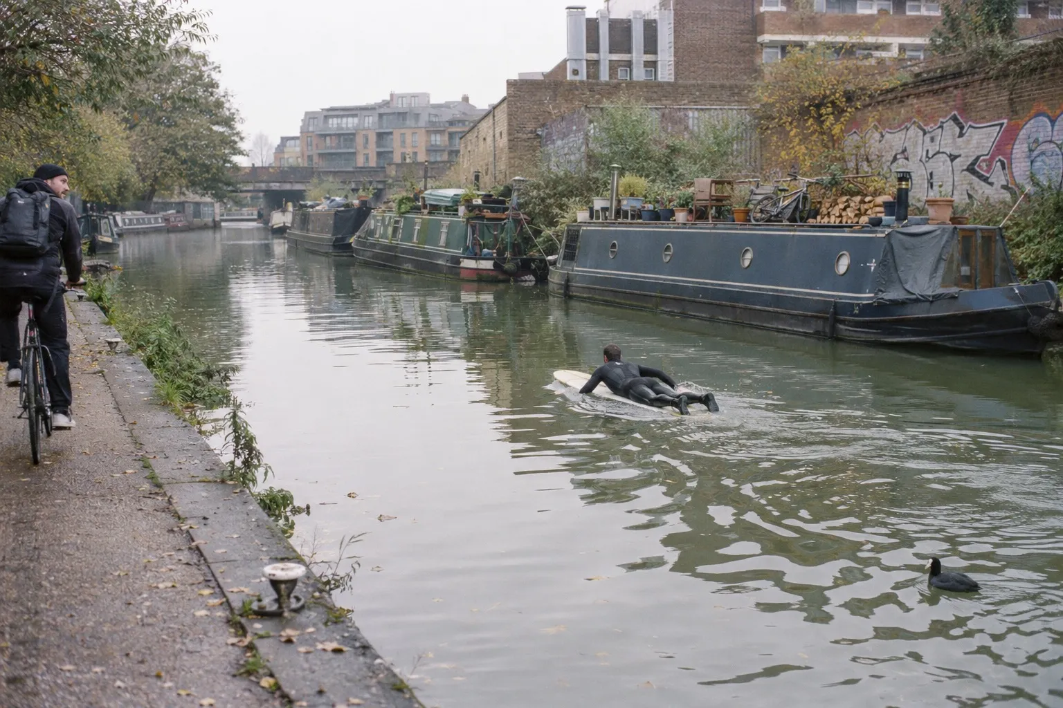 A surfer paddles a longboard past narrowboats on Regent's Canal