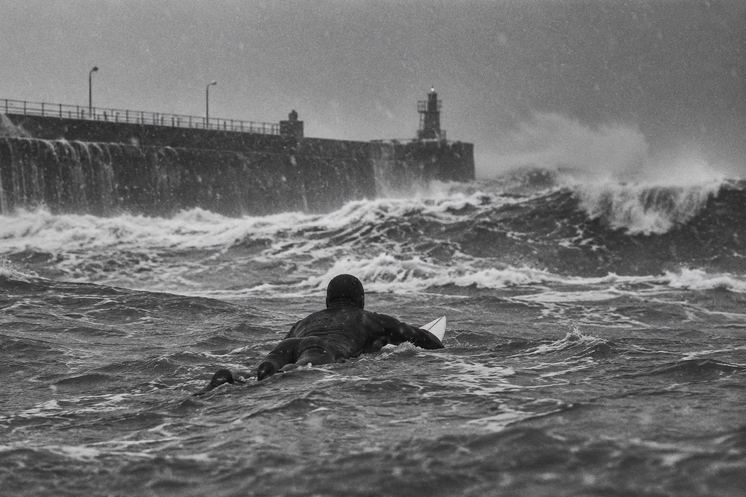 A surfer paddles out into a grey winter sea beside a harbour wall