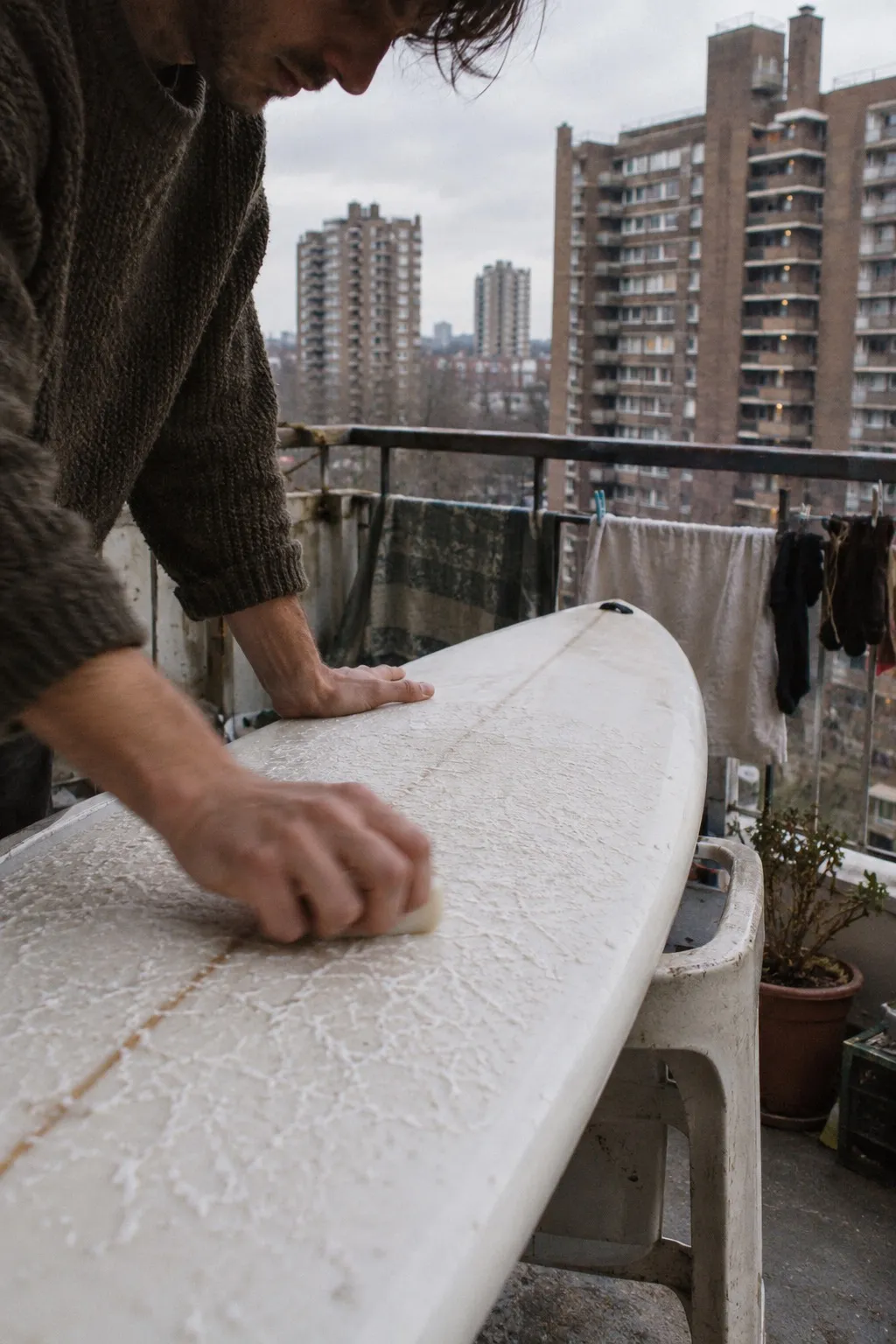 Hands waxing a board on a council estate balcony